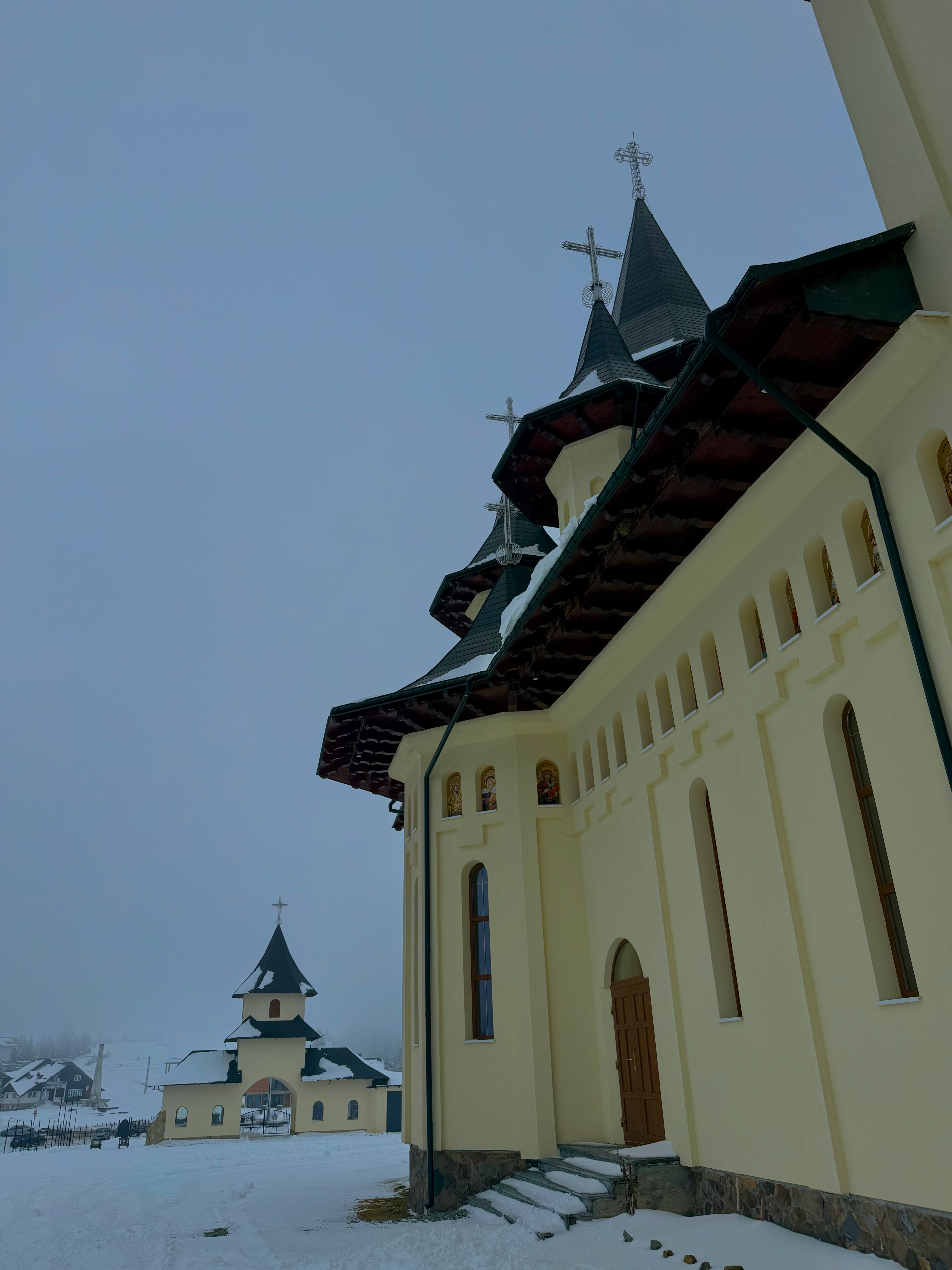 Carpathian Orthodox church with layered spires rising through winter mist, fresh snow on the ground
