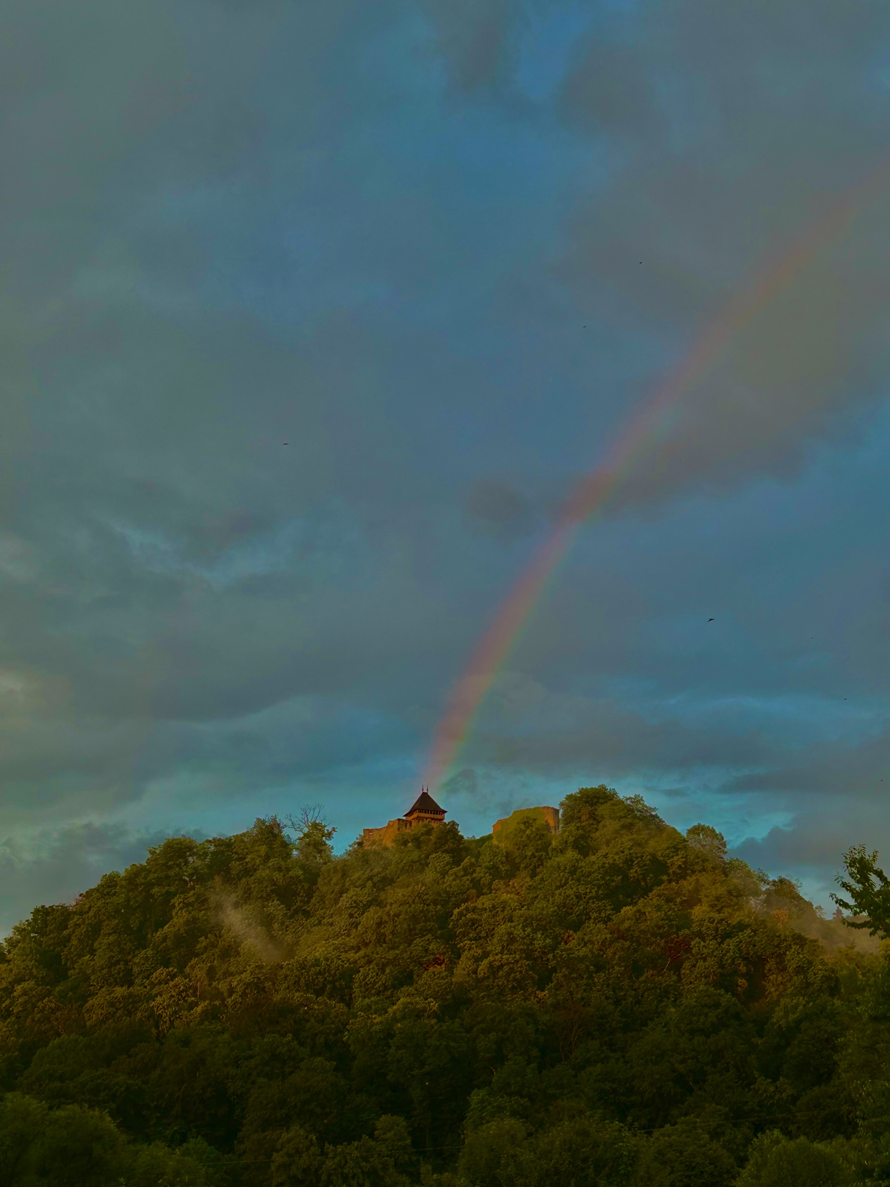 Nevytske Castle ruins on a volcanic hilltop with rainbow arcing through storm clouds, Zakarpattia