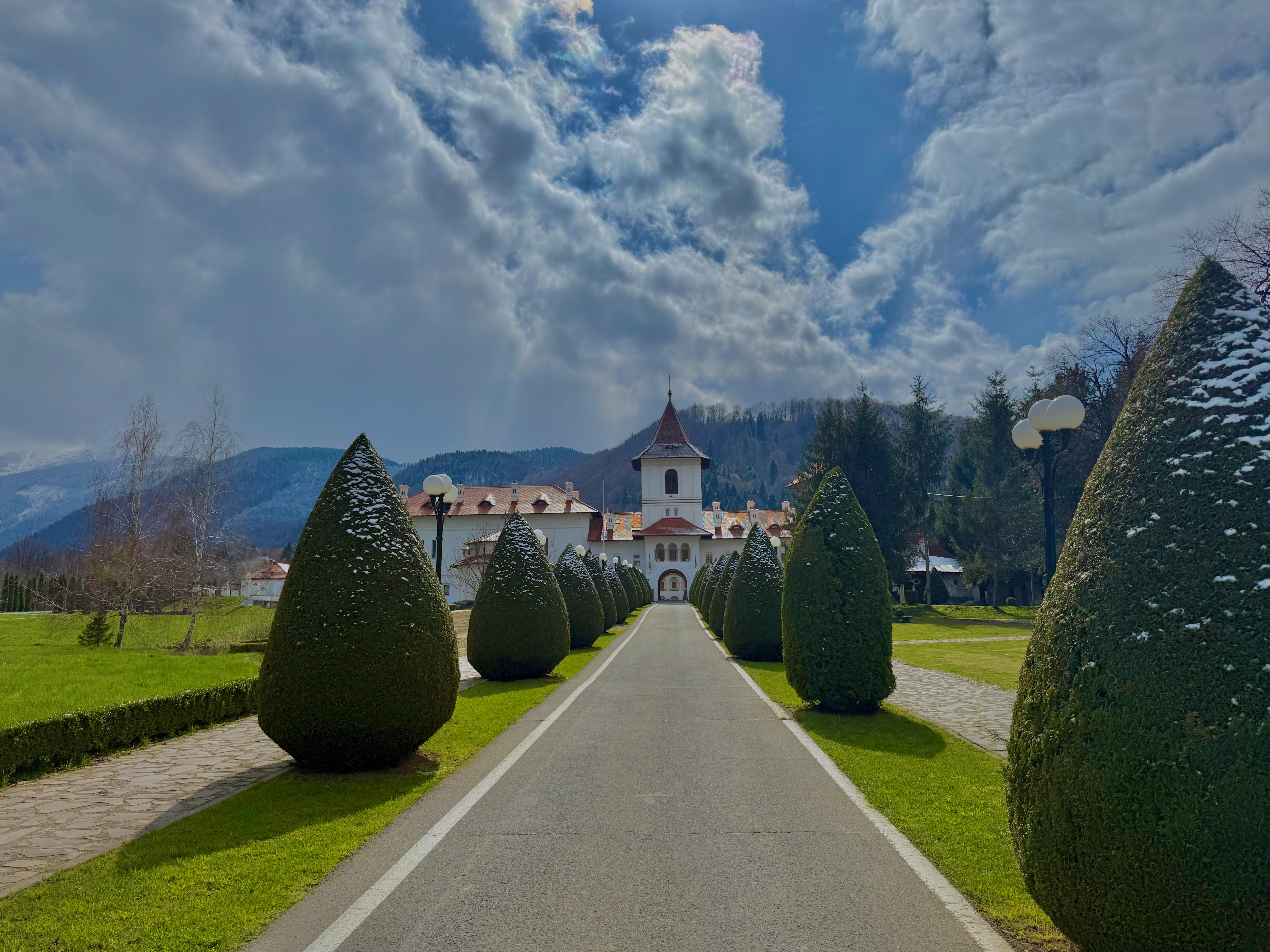 Tree-lined path leading to a Carpathian monastery with mountains beyond
