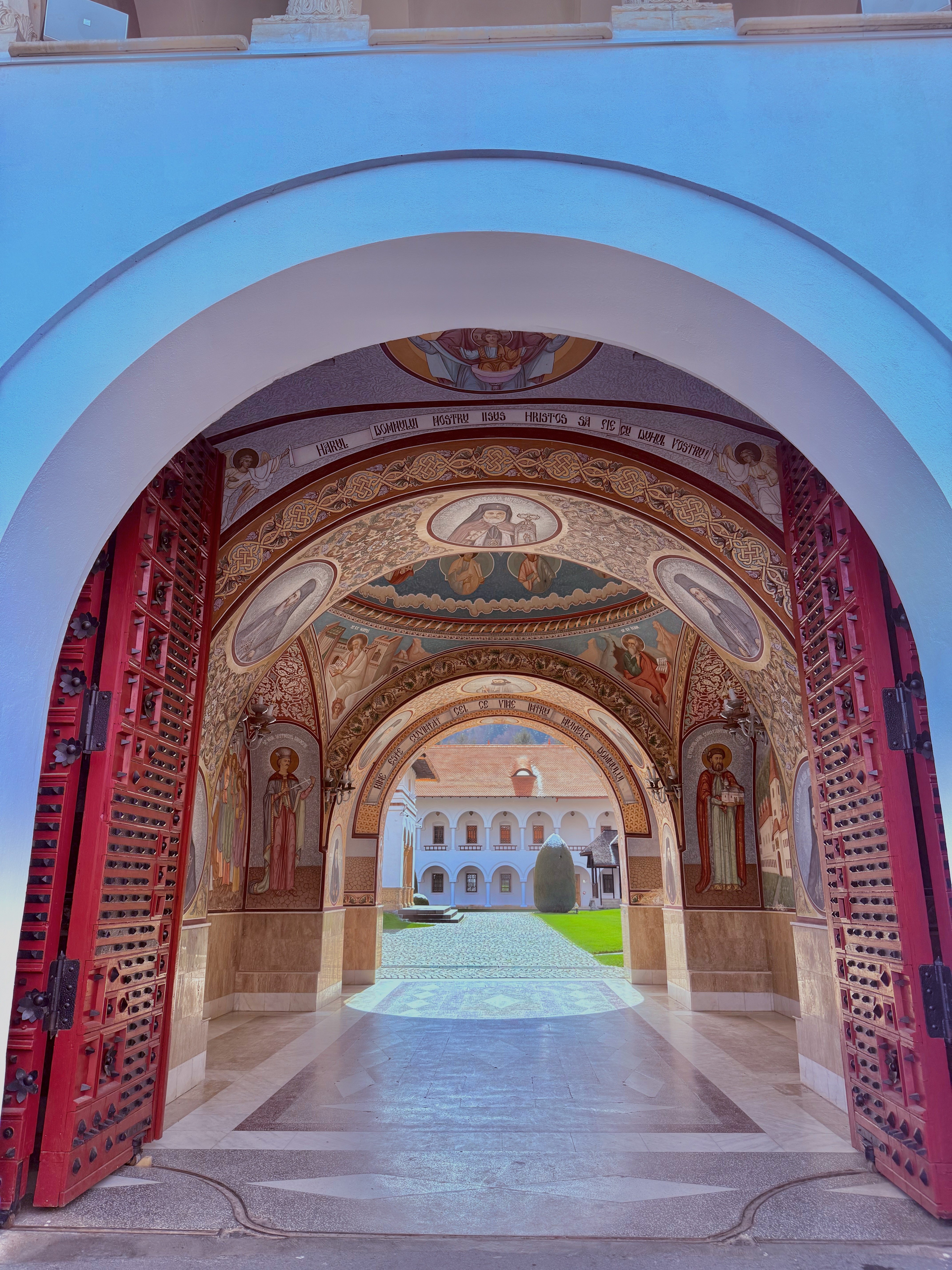 Painted arch gateway opening into a monastery courtyard with frescoed ceilings