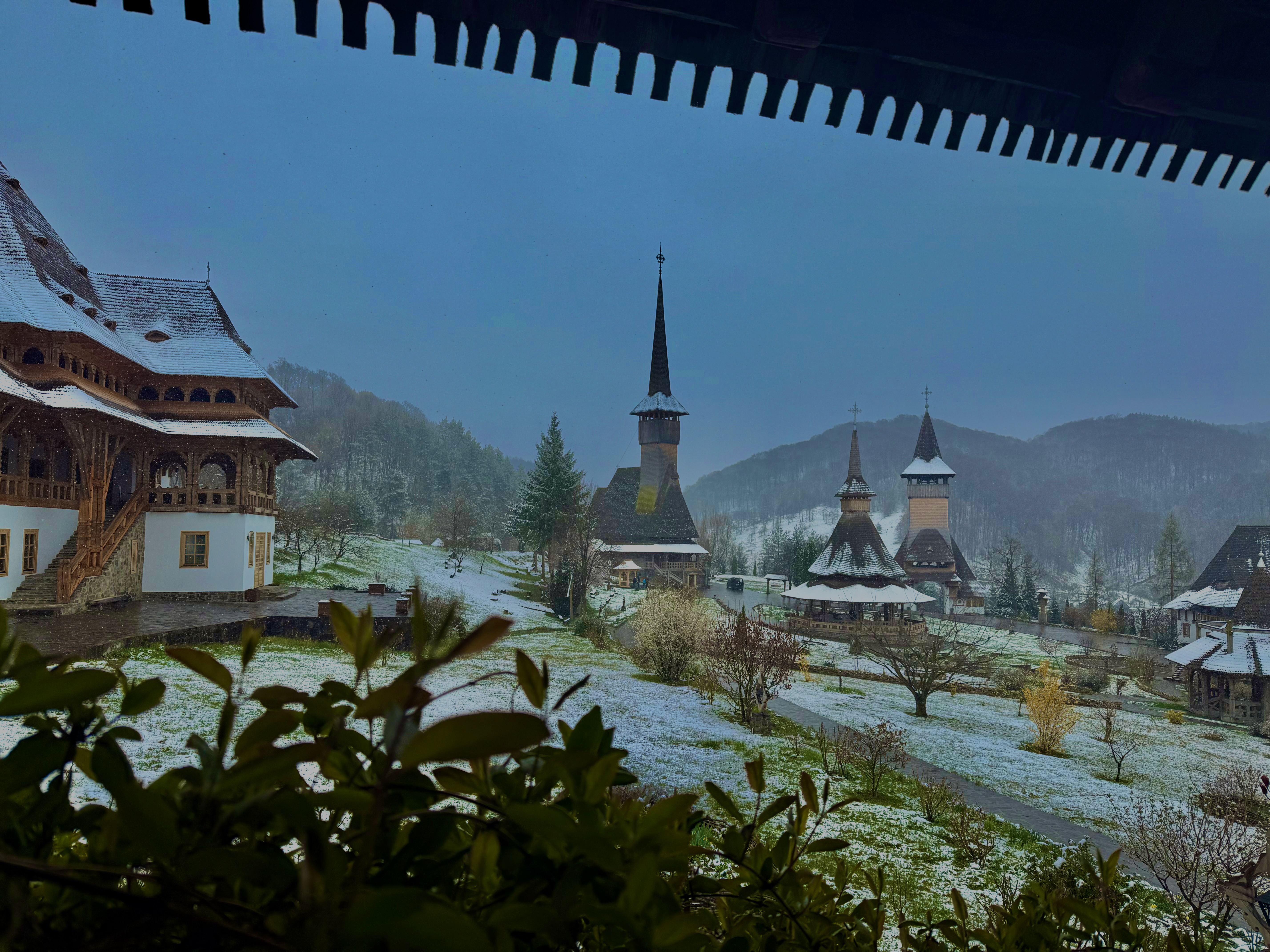 Bârsana monastery complex seen through a covered wooden walkway, snow dusting the grounds and spires beyond