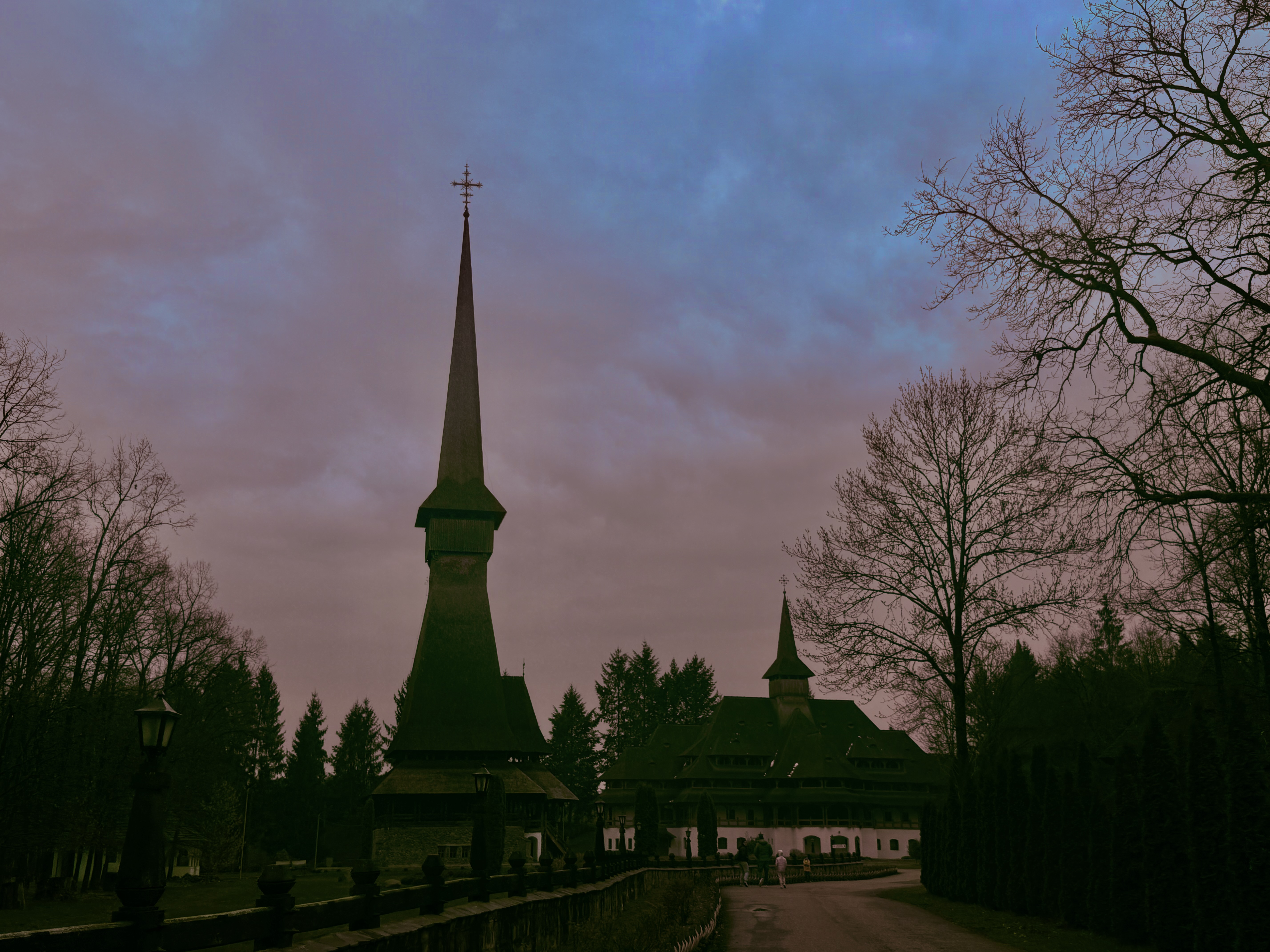 Tall wooden church spire silhouetted against a violet dusk sky, flanked by bare winter trees